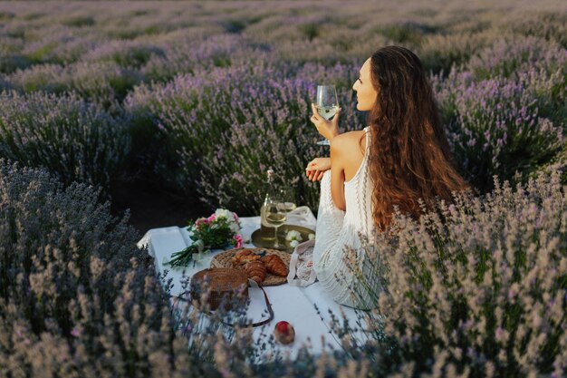 A woman sits in a field of lavender and holds a wine glass.