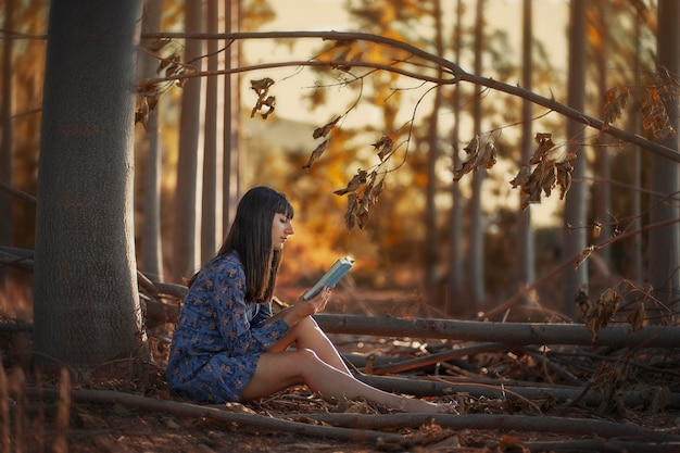 A woman sits in a forest reading a book.