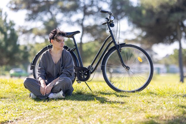 A woman sits on the grass next to a black bicycle