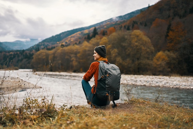 Woman sits on the grass in the mountains near the river and autumn landscape