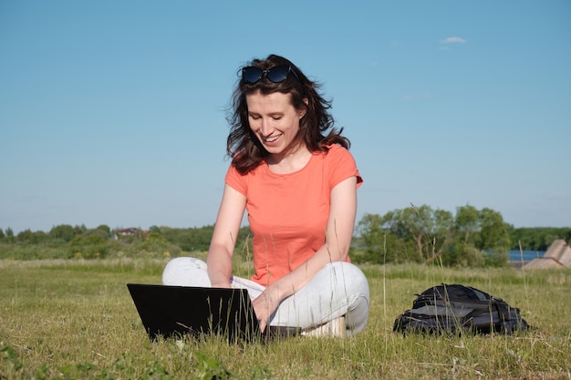 Woman sits on the grass and uses a laptop