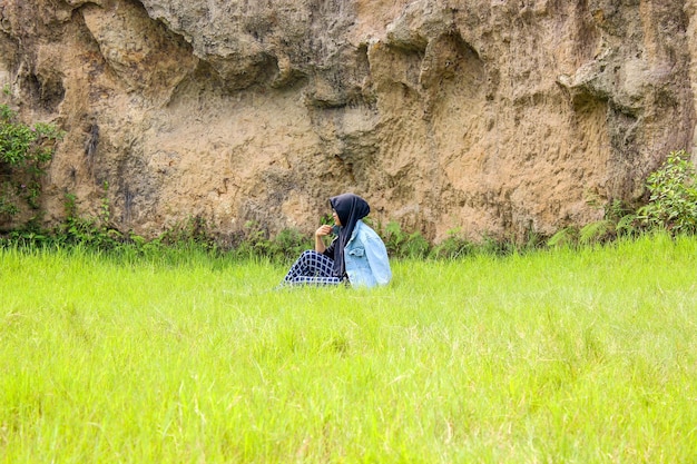 A woman sits on green grass against a large rock background