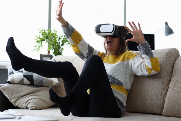 La donna si siede a casa sul divano utilizza la realtà virtuale