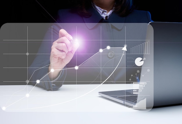 A woman sits at a laptop in front of a holographic chart with growing indicators. Business development, high financial performance, success.