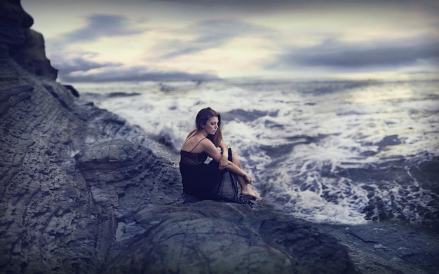 a woman sits on a large rock in the ocean