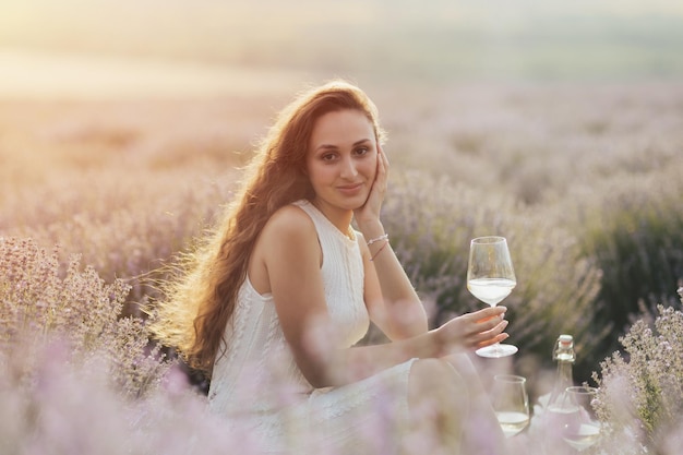 A woman sits in a lavender field and holds a glass of wine.