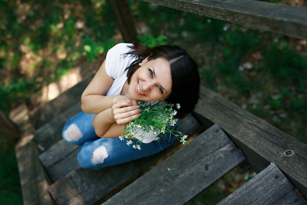 A woman sits on an old wooden staircase and holds a bouquet of wildflowers.