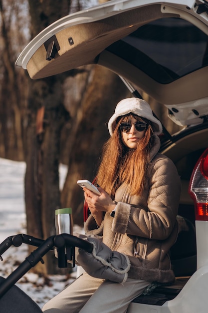 a woman sits in the open trunk of a jeep in winter while a child sleeps in a stroller