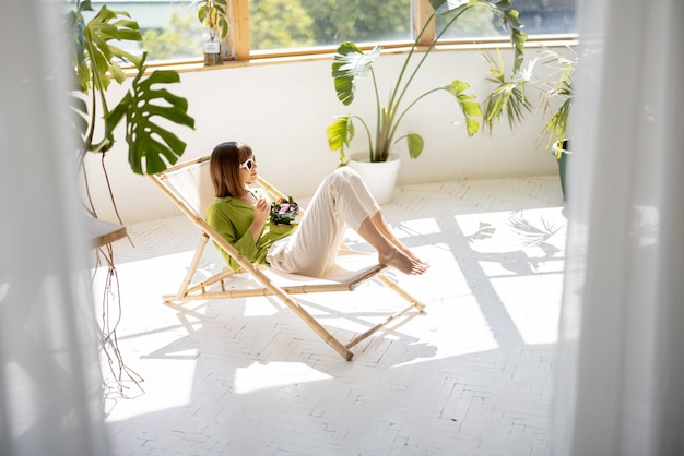 Woman sits relaxed with a drink in room with plants