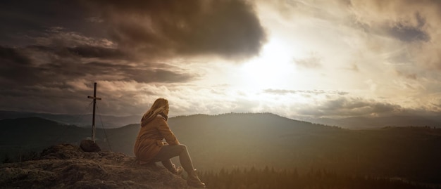 Женщина сидит на скале перед горой.