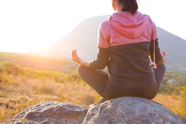 A woman sits on a rock in the lotus position