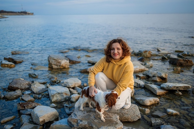 Foto una donna siede su una roccia con il suo cane sulla riva.