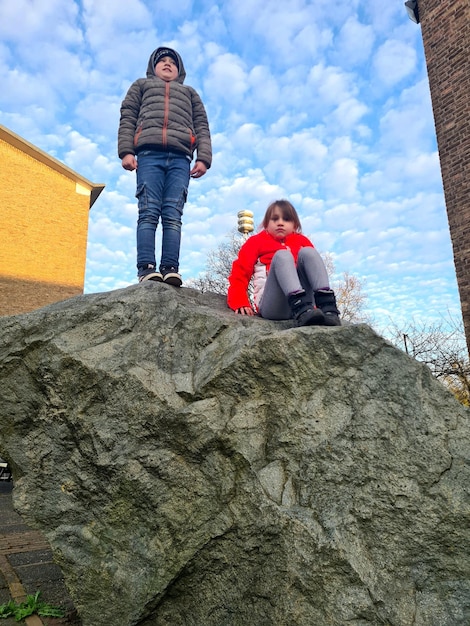 A woman sits on a rock with a man in a red jacket.