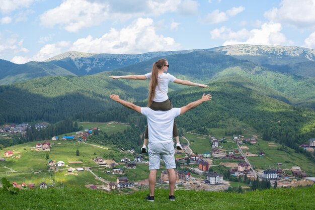 woman sits on the shoulders of the guy and admire the mountains. Back view