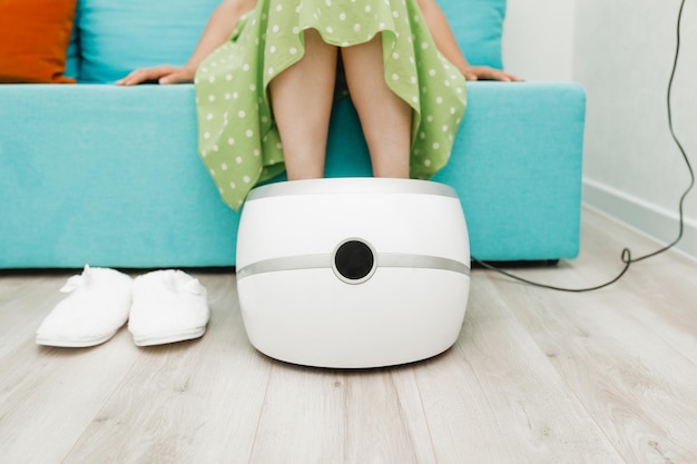 woman sits on the sofa and uses a foot massager for relaxation which helps relieve pain and improve blood circulation