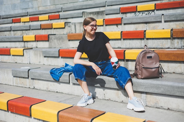 Woman sits on steps and holds a disposable cup of coffee