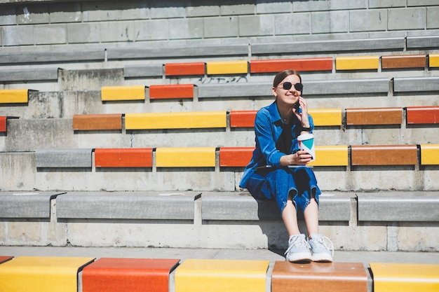 Woman sits on steps and holds a disposable cup of coffee