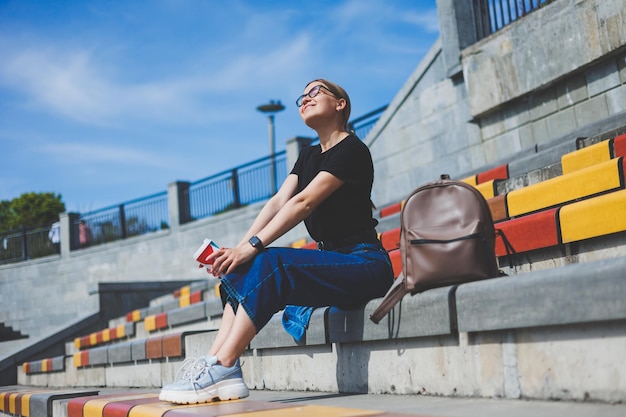 Woman sits on steps and holds a disposable cup of coffee