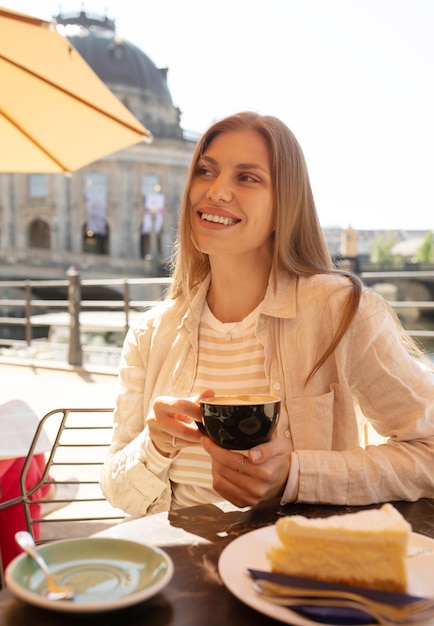 A woman sits at a table in a cafe, holding a cup of coffee.