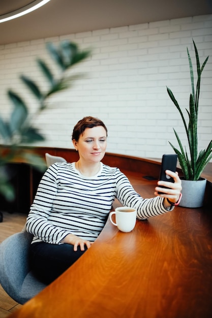 Photo a woman sits at a table in a modern office and communicates on a smartphone