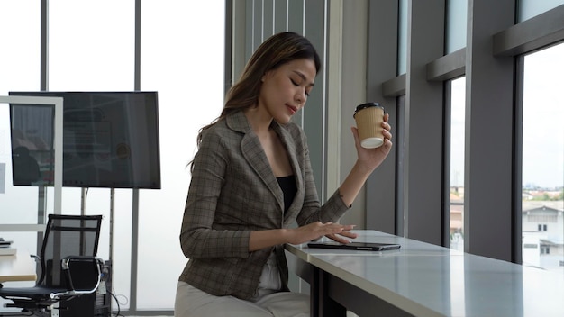 A woman sits at a table in an office, holding a coffee cup.