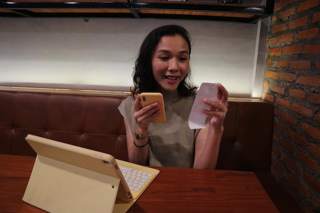 A woman sits at a table with a laptop and a phone that says'i'm a computer '