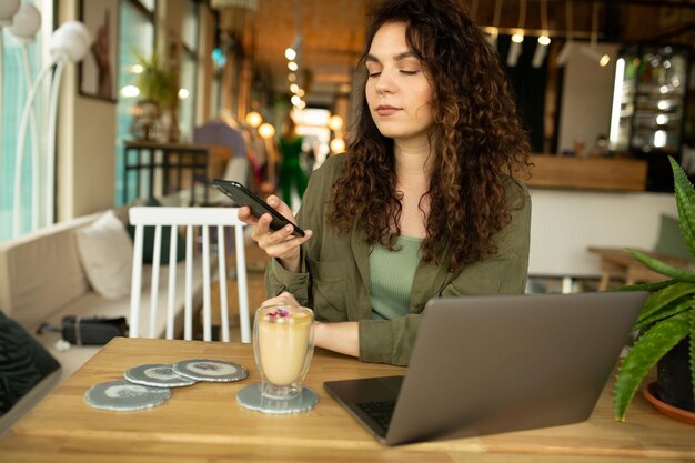 A woman sits at a table with a laptop and a phone.