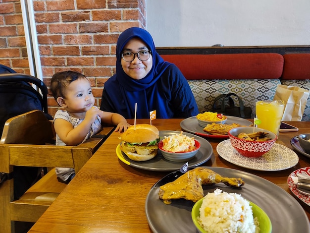 Photo a woman sits at a table with a plate of food and a child wearing a hijab.