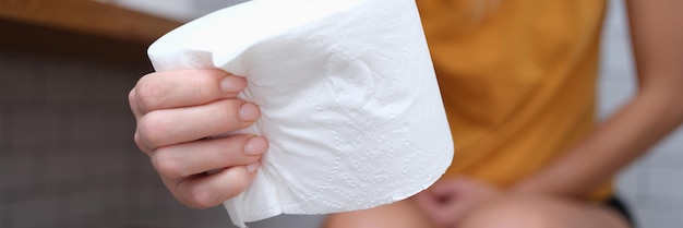 Woman sits on toilet and holds toilet paper in hands