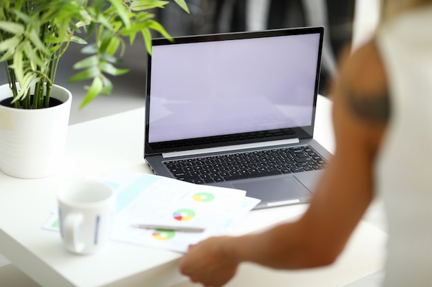 A woman sits at a white table in front of a working laptop documents with a diagram are on the