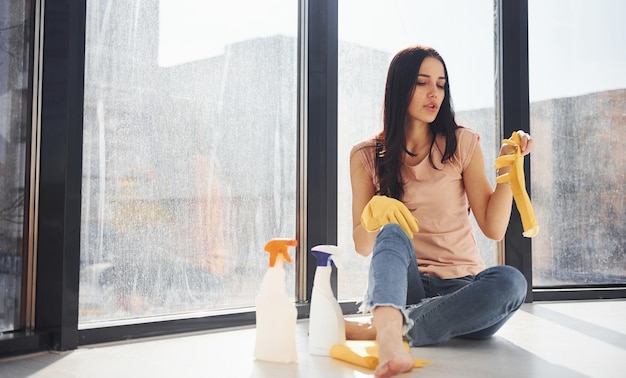 Photo woman sits on window sill with bottles of cleaning spray and with gloves