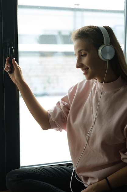 A woman sits on the windowsill in headphones