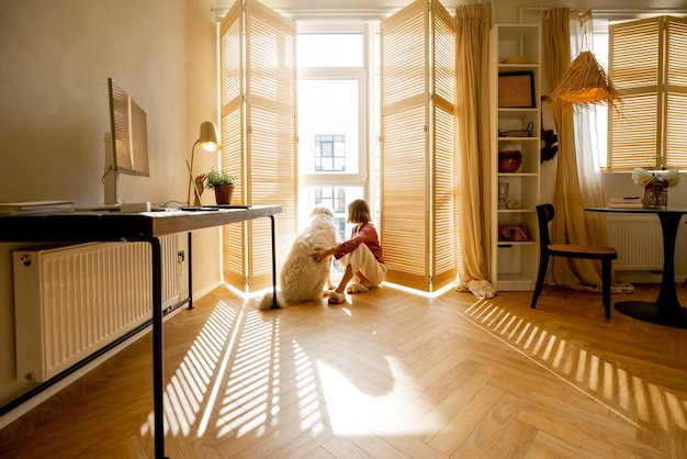 Woman sits with dog by the window blinds at home