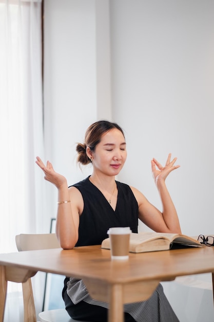 Photo a woman sits at a wooden table with a book and coffee practicing mindfulness meditation in a bright serene room