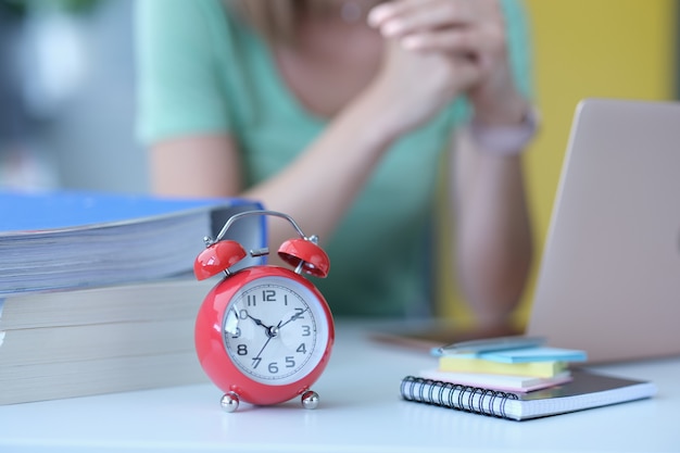 Woman sits at workplace next to alarm clock at ten in morning