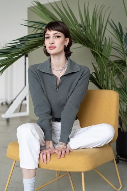 A woman sits on a yellow chair in front of a plant