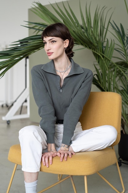 A woman sits on a yellow chair in front of a plant