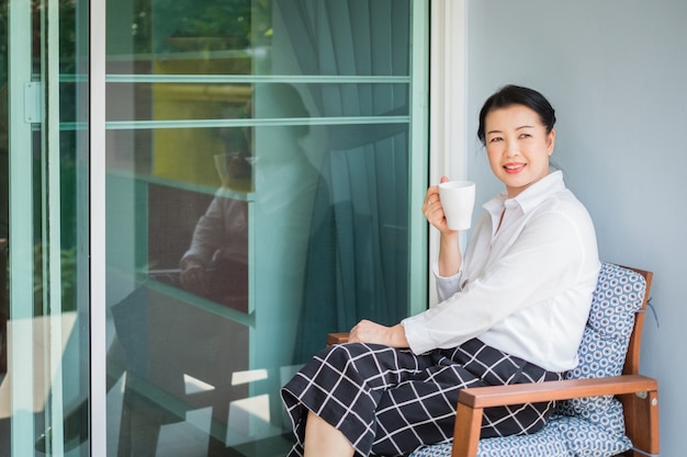 Woman sitting in armchair and drinking coffee at home in the morning