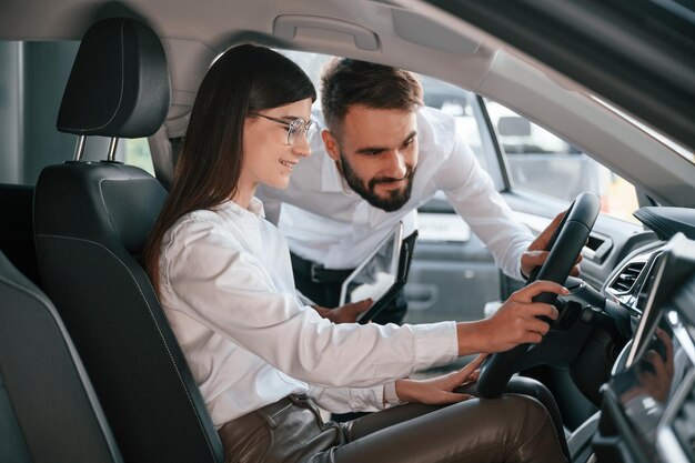 Woman sitting in the automobile Man in white clothes are in the car dealership