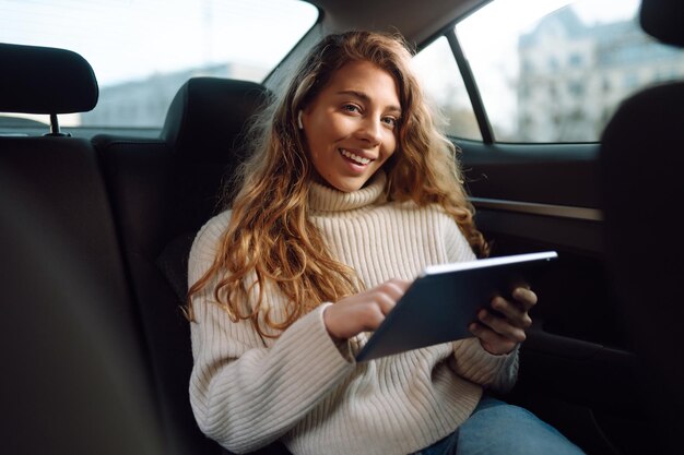 태블릿을 손에 들고 차 뒷좌석에 앉아 있는 여성 비즈니스 택시 기술 온라인 콘서트