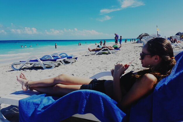 Woman sitting on beach against blue sky