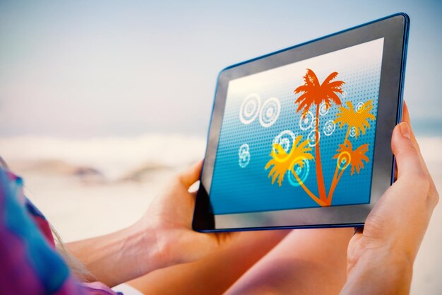Photo woman sitting on beach in deck chair using tablet pc showing digitally generated palm tree background