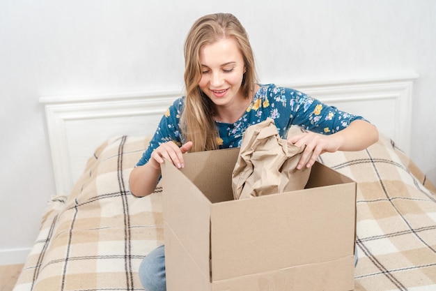 Woman sitting on bed unpacking cardboard box at home Delivering parcel