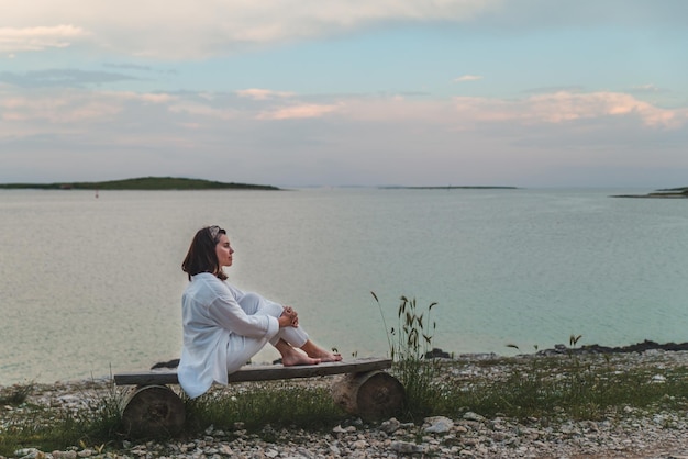 海に沈む夕日を見ながらベンチに座っている女性