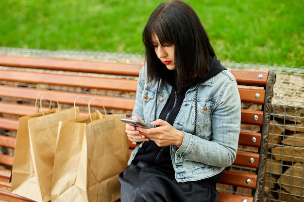 買い物の後、紙の買い物袋を持って公園のベンチに座っている女性