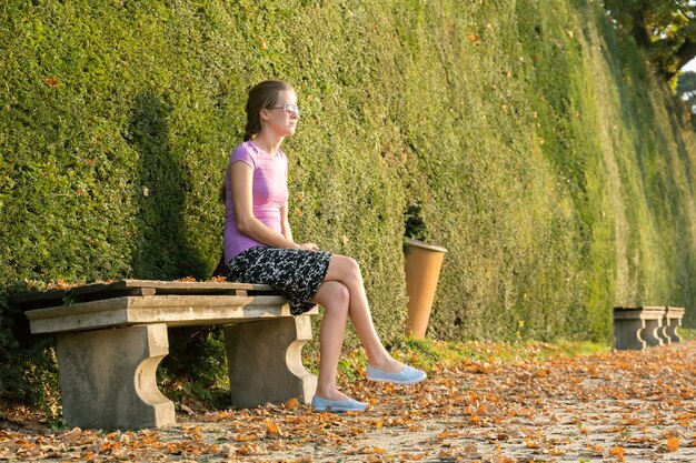 A woman sitting on a bench in summer park.