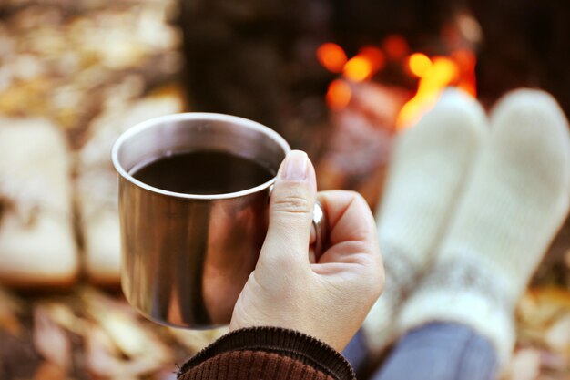 一杯のコーヒーのクローズアップで火のそばに座っている女性