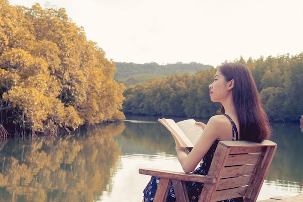 Photo woman sitting on book by lake against trees