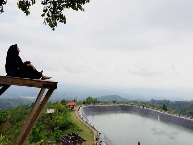 Woman  sitting on bridge over river against sky