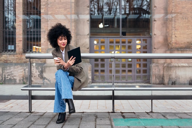 Woman sitting at the bus stop consulting a tablet